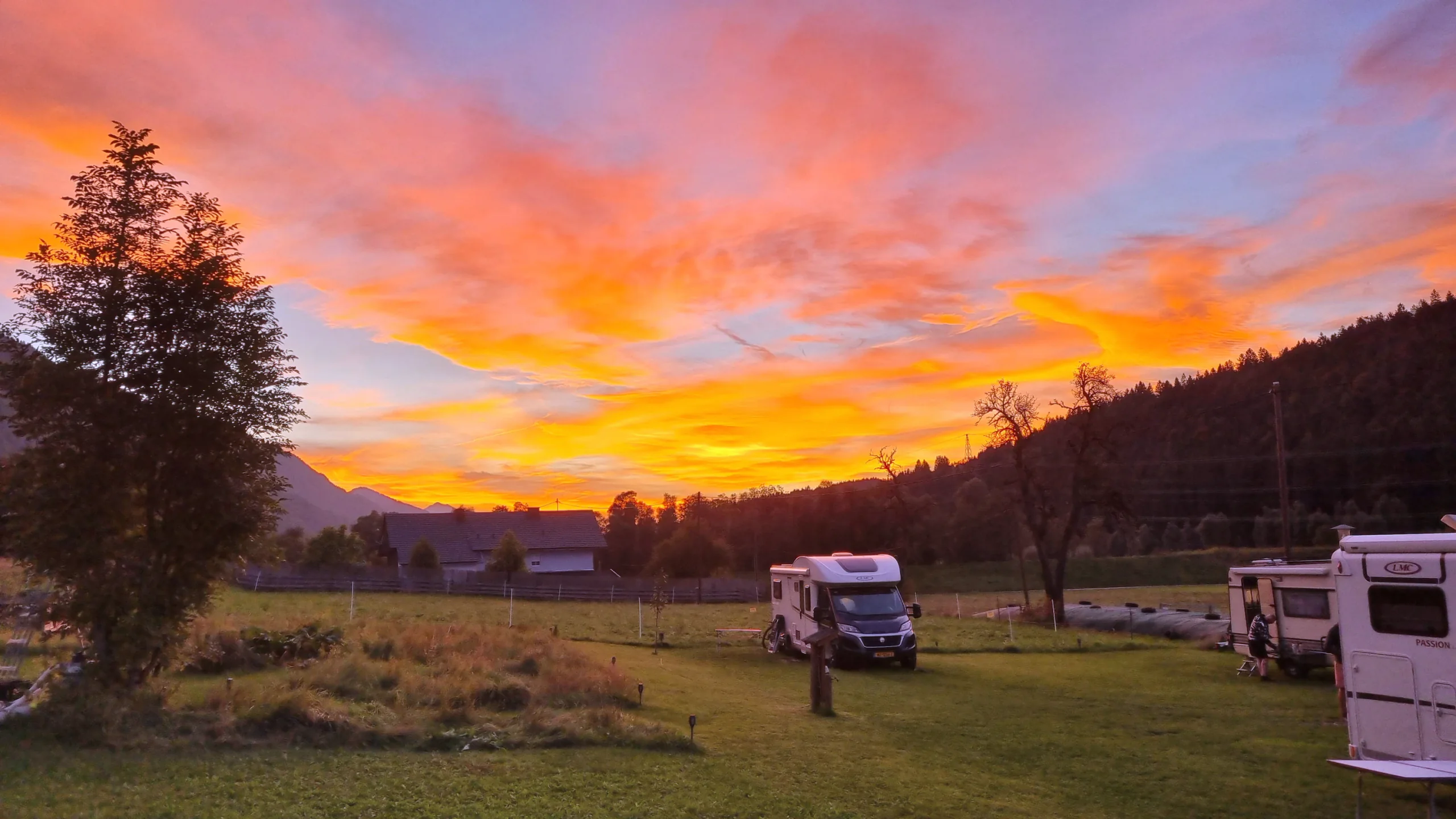 Leuchtend oranger Abendhimmel über der Stellplatzwiese mit zwei Wohnmobilen
