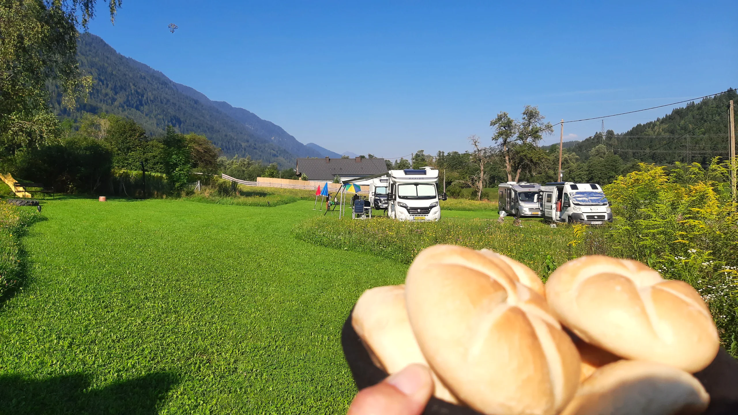 Frische Brötchen in der Hand, dahinter die Wohnmobile auf der Morgenwiese