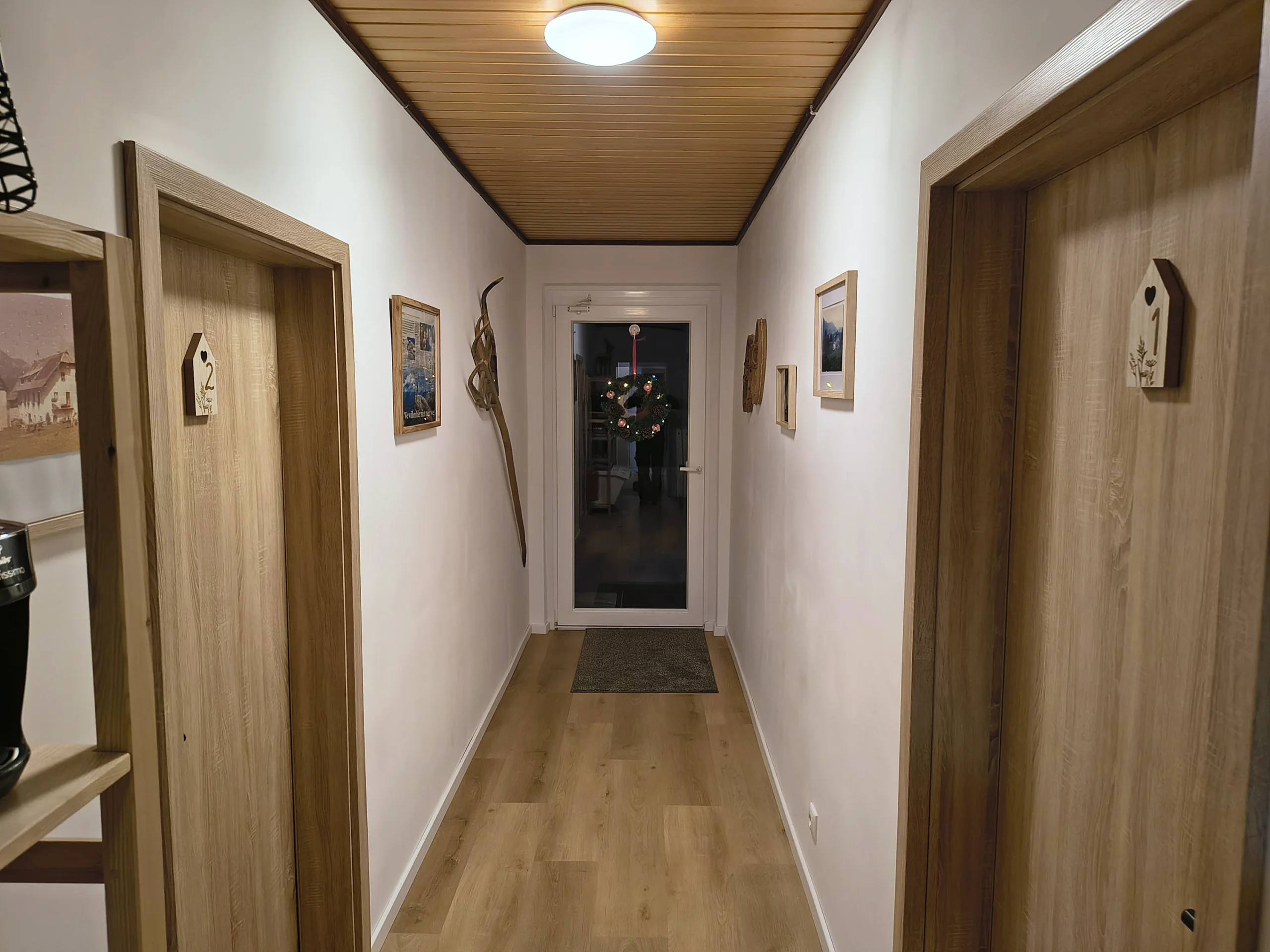 Flur mit Holzdecke, links und rechts die nummerierten Türen zu den beiden Wohnungen, am Ende der Hauseingang