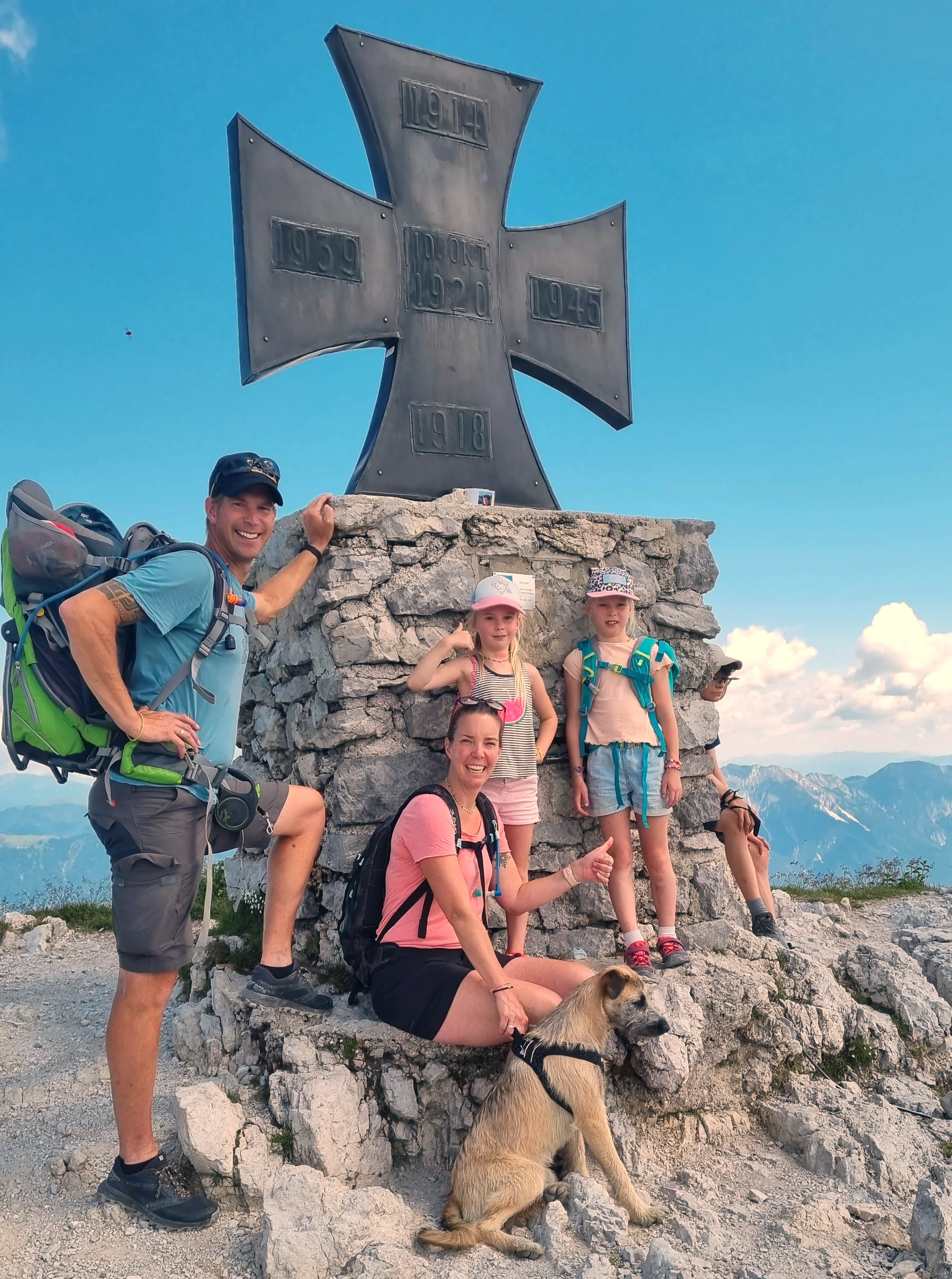 Familie de Jong rastet mit ihrem Hund am Gipfelkreuz einer Bergwanderung