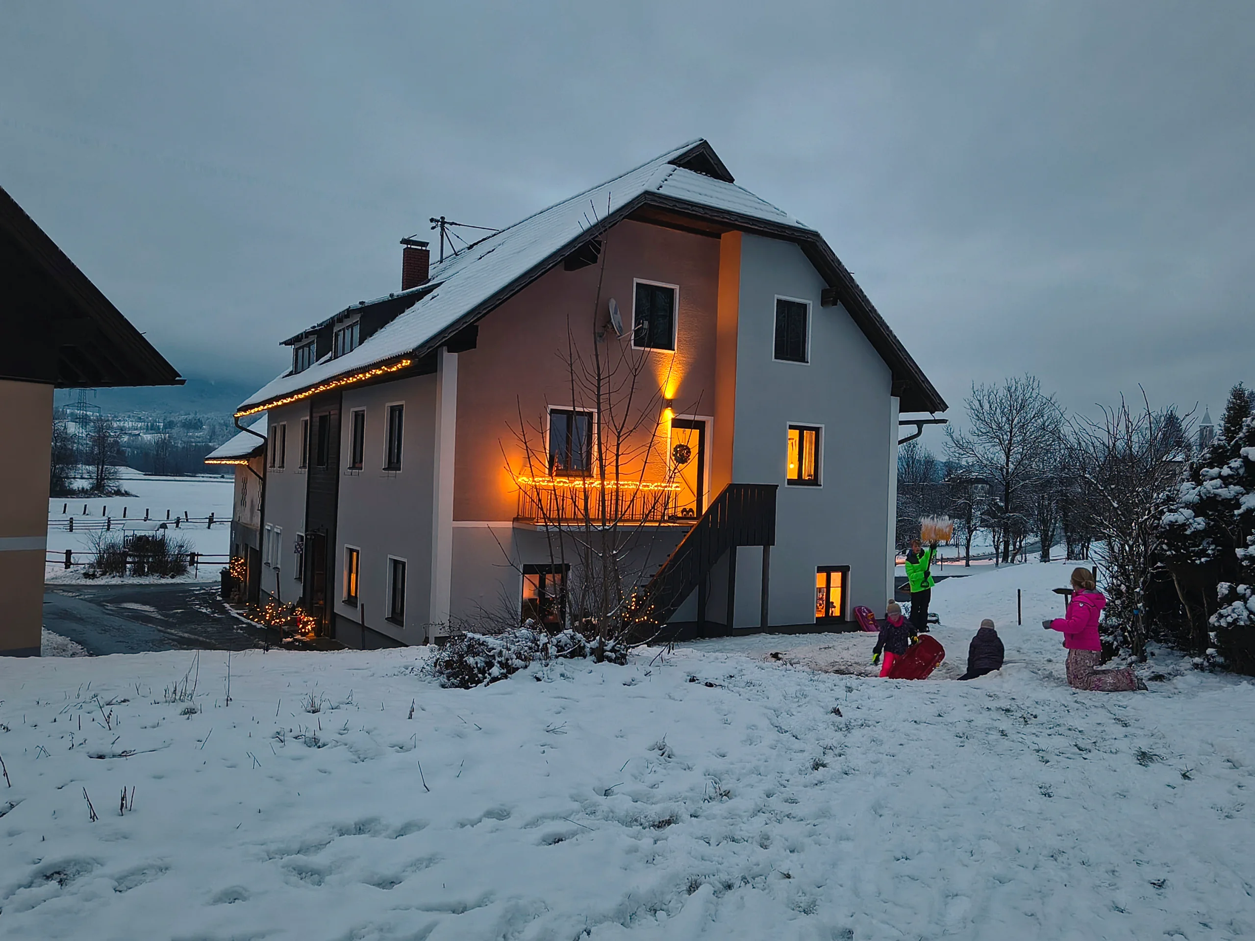 Haus Nampolach zur blauen Stunde im Schnee, die Fenster warm erleuchtet und Lichterketten am Dach
