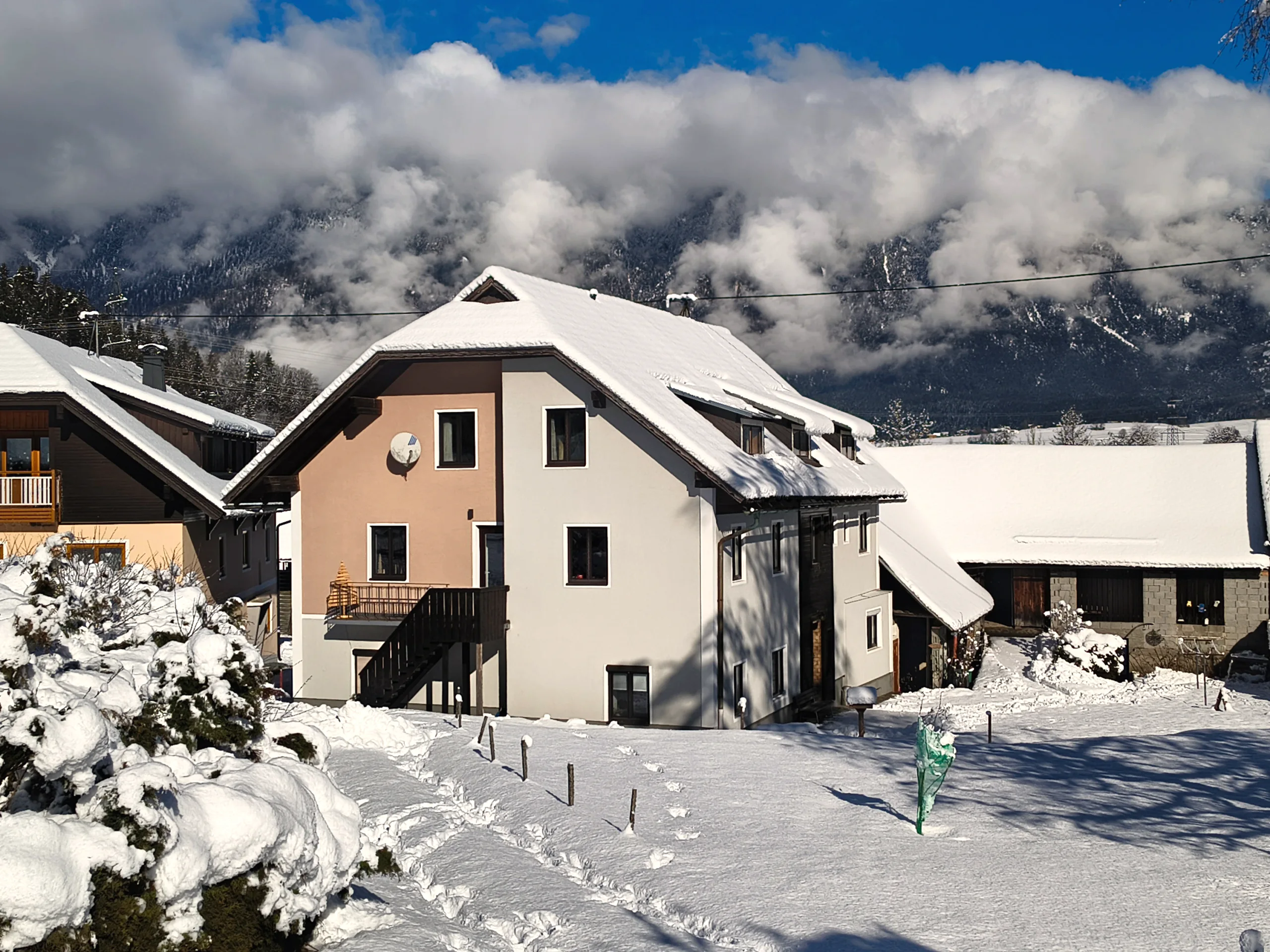 Haus Nampolach im Schnee unter blauem Himmel, davor die Außentreppe und ein kahler Baum