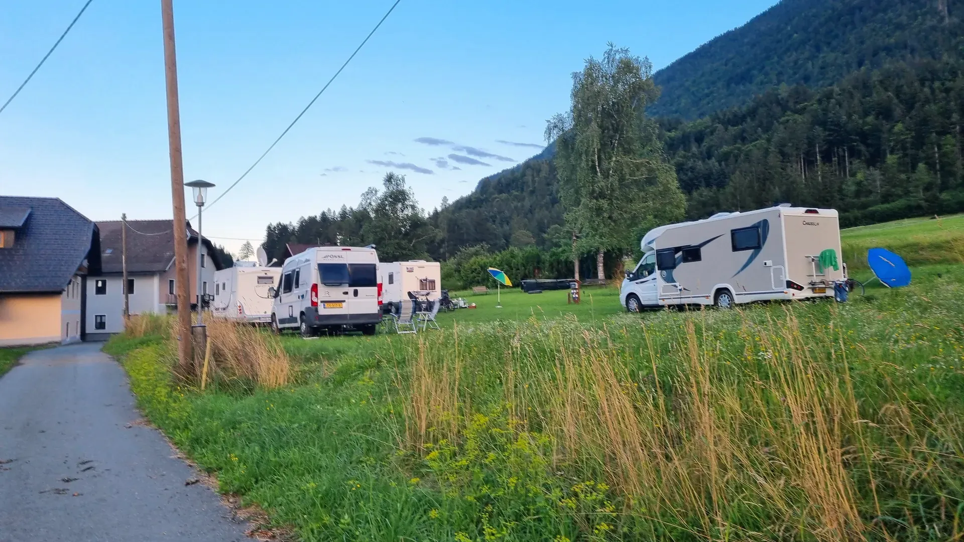 Abendstimmung über der Wiese in Nampolach mit Wohnmobilen und bewaldetem Berghang